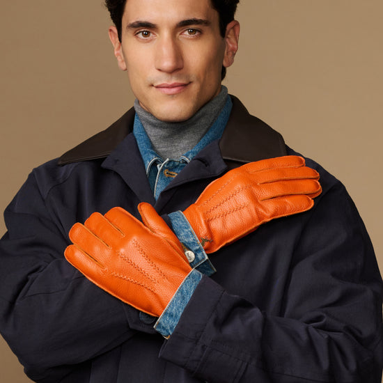 Men’s orange deerskin leather gloves with blue lining, worn under a dark coat