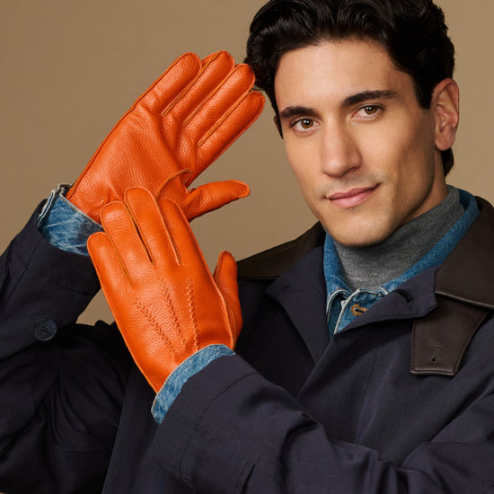 Men’s orange leather gloves with blue lining cuff, hand posed forward