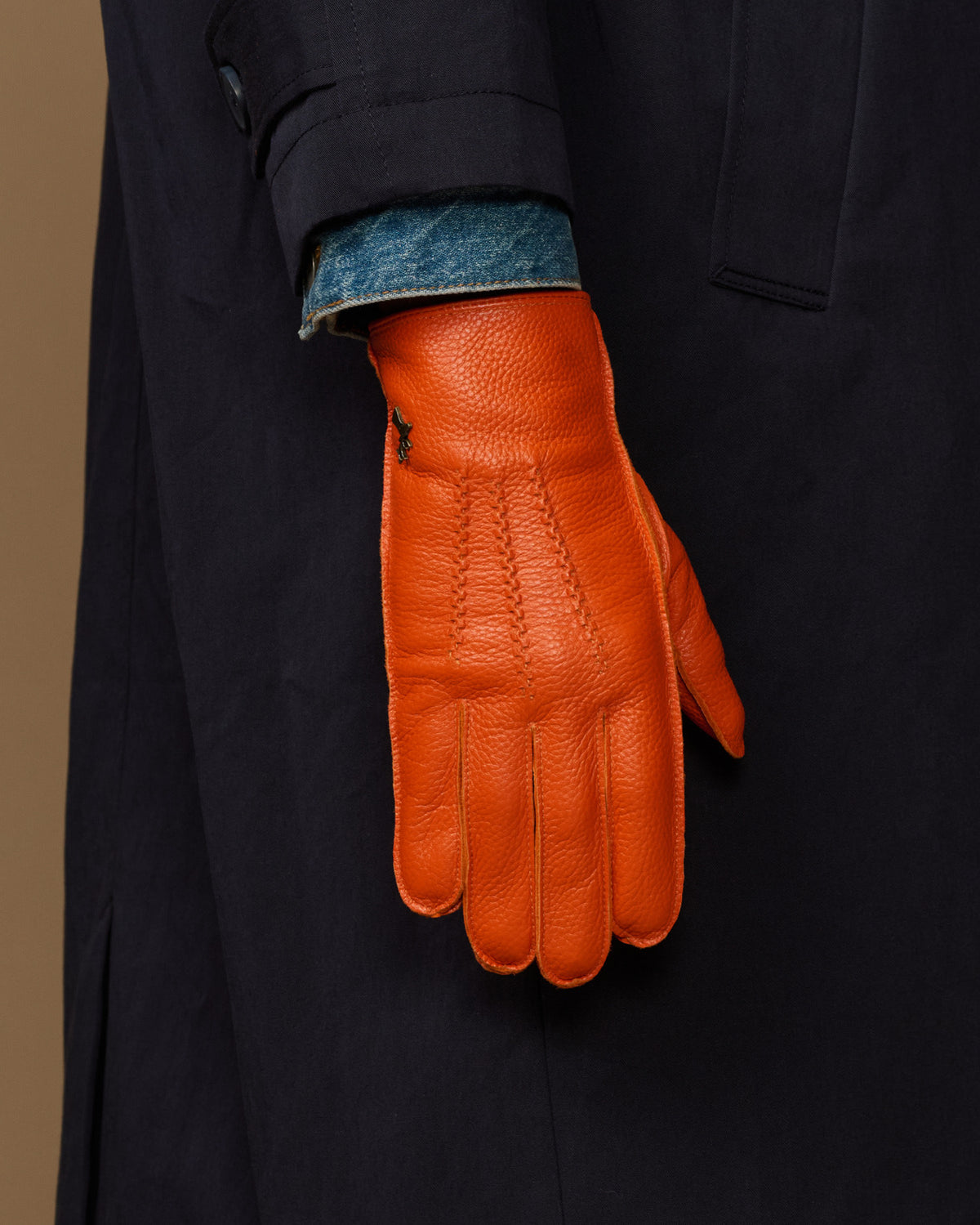 Orange leather gloves with blue cuff lining on dark sleeve, side view