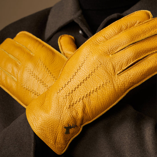 Yellow leather gloves held up close-up, visible stitched seams and texture