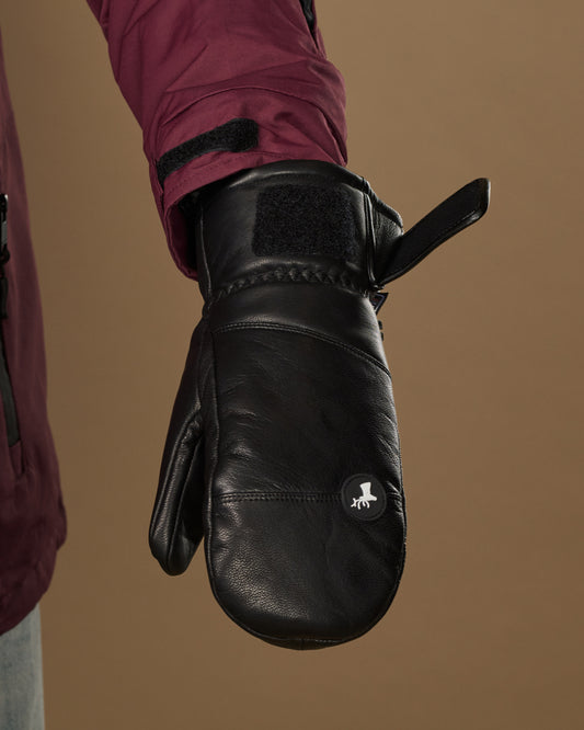 Black leather mitten close-up showing a wrist strap, stitched cuff, and logo patch.