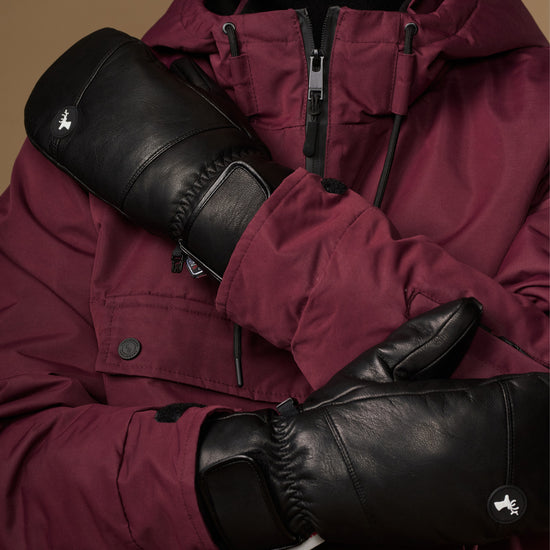 Close-up of black leather mittens with gathered cuffs and logo patches.