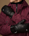 Close-up of black leather mittens with gathered cuffs and logo patches.