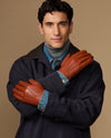 Men's cognac leather gloves with blue lining, arms crossed in front of coat