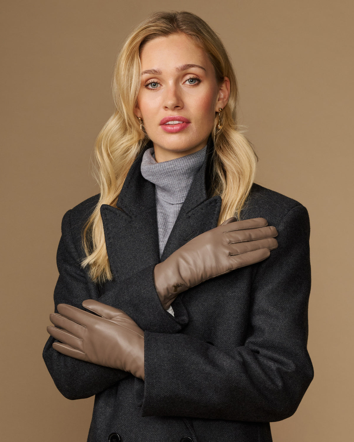 Pair of women’s taupe leather gloves with stitched seams, worn with dark outerwear