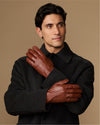 Cognac leather gloves with fleece-lined cuffs, worn by model with both hands raised