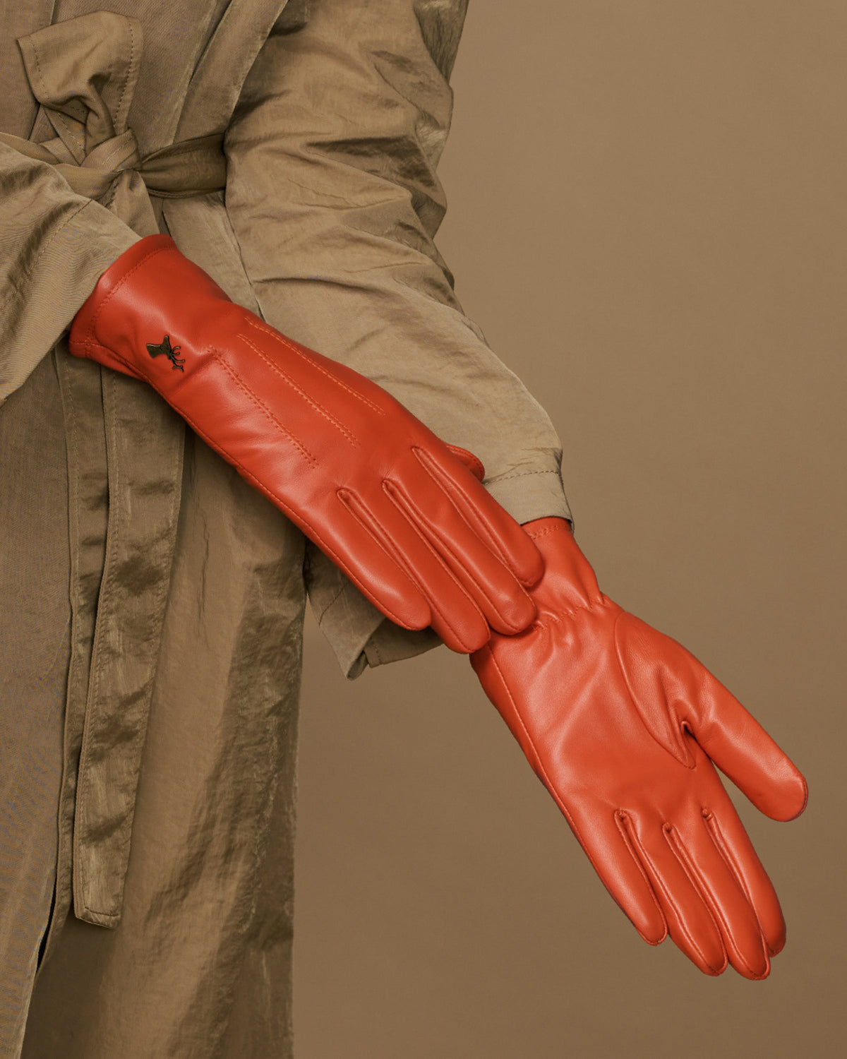 Orange sheepskin leather glove laid across a jacket sleeve, showing stitched fingers