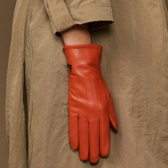 Orange sheepskin leather glove with fleece lining, hanging from a jacket cuff