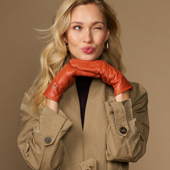 Orange sheepskin leather gloves with fleece lining, worn with arms crossed at chest
