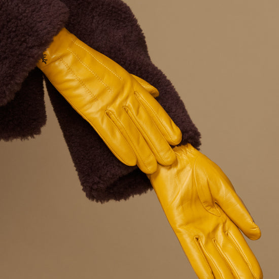 Close-up of yellow leather gloves with stitched fingers and dark plush cuff lining