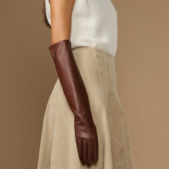 Elbow-length brown leather glove worn at side, with soft cuff detail.