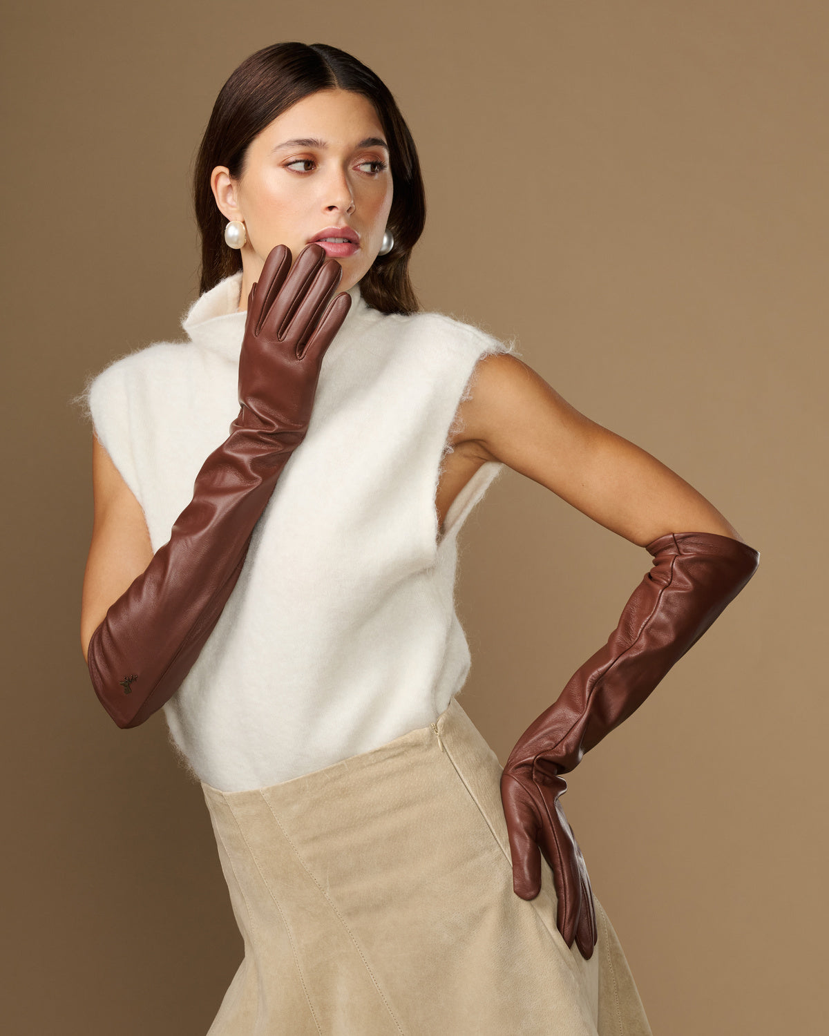 Women’s elbow-length brown leather gloves, one raised near face while wearing.
