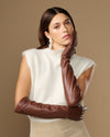 Women’s brown leather elbow gloves with smooth finish, worn across chest.