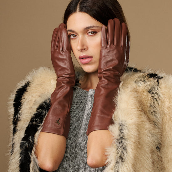 Women's brown below-elbow leather gloves with silk lining, close hands near face