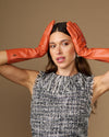 Women’s orange leather gloves raised near head, close fit at wrists