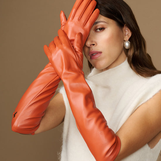 Close-up of orange leather elbow gloves with smooth, glossy finish and finger details