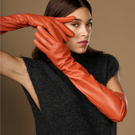 Orange lambskin leather gloves with silk lining and touchscreen tips, close-up on hands
