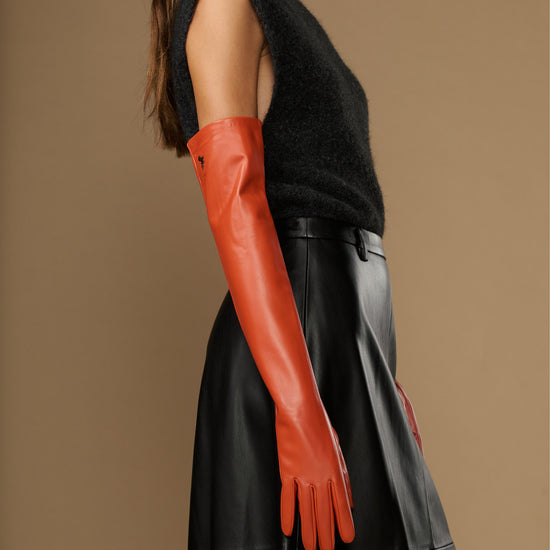 Orange leather gloves with fitted cuffs; silk lining and touchscreen feature visible on wrist