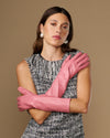 Pink below-elbow leather gloves, smooth fitted style, arms crossed with gloves visible