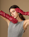 Pair of red leather gloves raised near face, showing knuckle shaping and slim fit