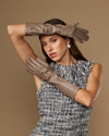 Taupe leather gloves with below-elbow cuff, smooth surface and stitched fingers on raised arms.