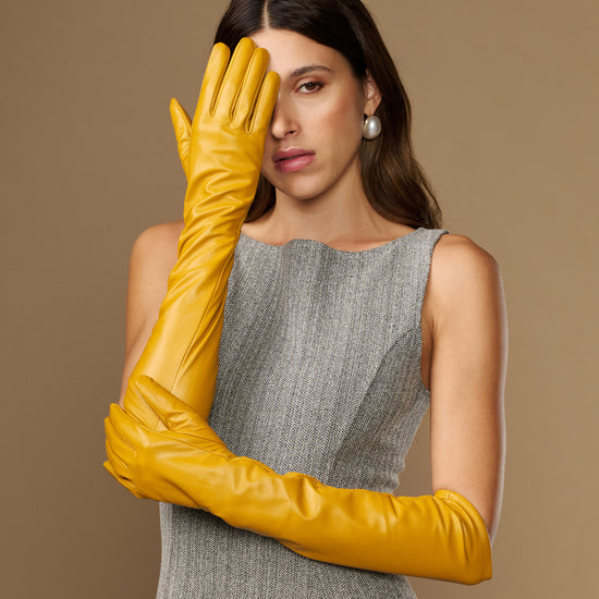 Yellow leather elbow gloves on model hands, one glove raised near face