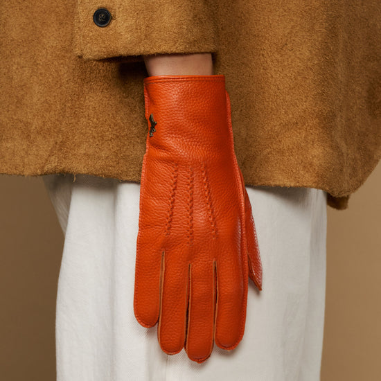 Orange leather glove with soft lined cuff and stitched fingertips, hanging from sleeve
