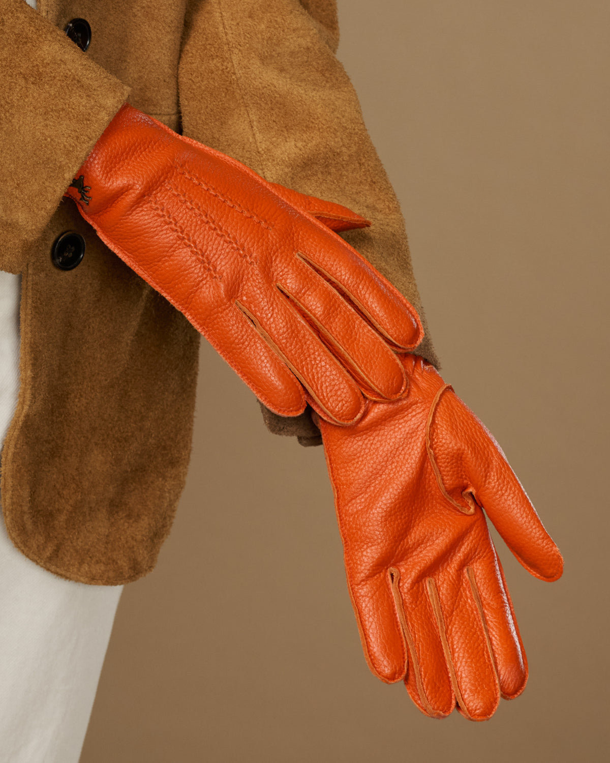 Orange leather glove close-up with textured stitching on knuckles and palm, extended hand