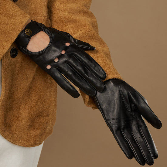 Black leather driving gloves with oval buckle emblem and button-studded cuff opening.